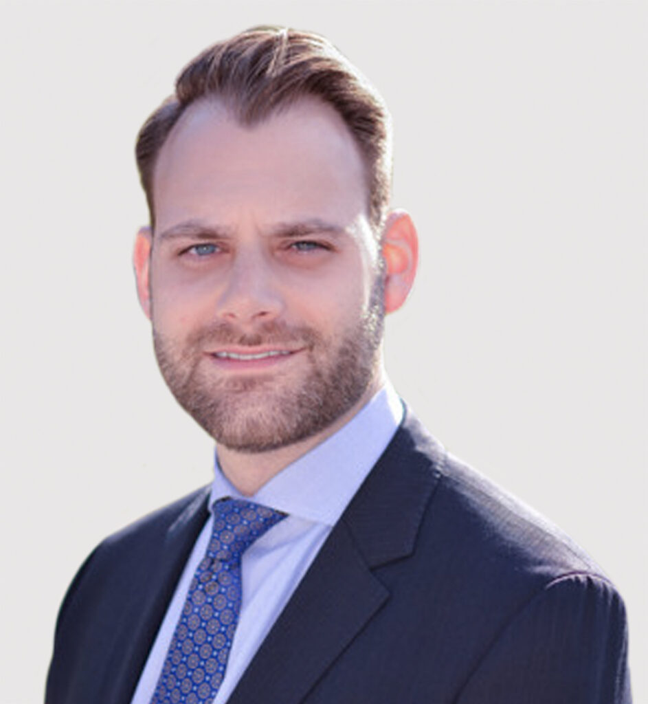 Portrait of Ari Laskin wearing a blue suit, light blue shirt and blue tie, against a light grey background.
