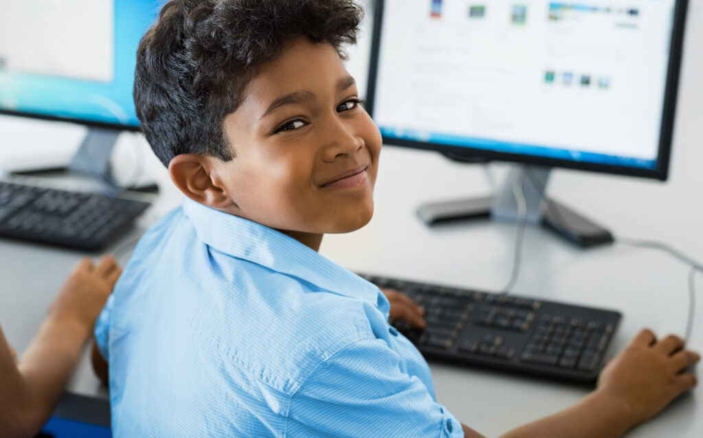 Un enfant assis à un bureau et travaillant sur un ordinateur jette un regard en arrière et sourit.