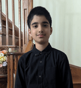 Grade 7 student with short dark hair, wearing a grey plaid shirt, standing upright and facing the camera. Photo centred on a blue graphic background.