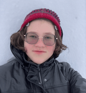 Grade 12 student with short brown hair, wearing glasses and a blue and white sweater, facing the camera. Photo centred on a blue graphic background.