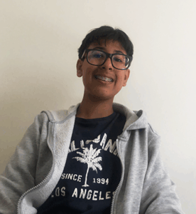 Grade 9 student with short dark hair, wearing glasses and a black hoodie, upright and facing the camera. Photo centred on a blue graphic background.