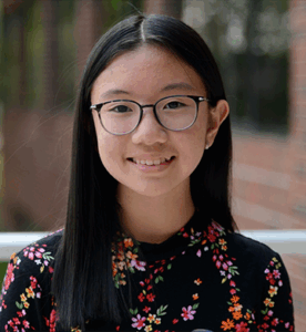 Grade 10 student with long dark hair, wearing glasses, upright and facing the camera. Photo centred on a blue graphic background.