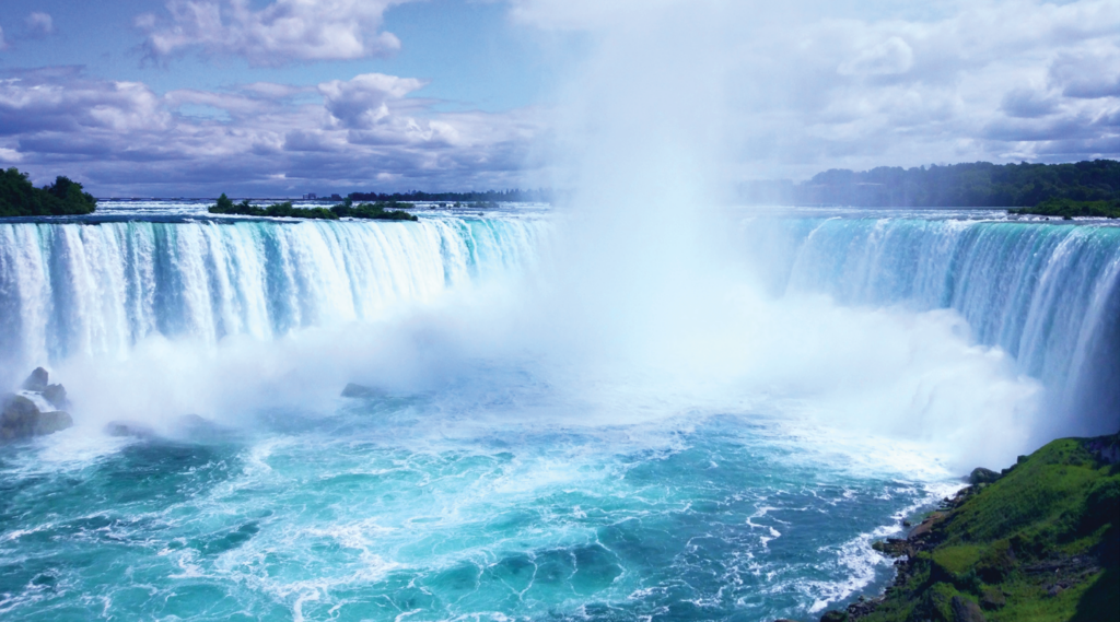 Wide-angle view of the Niagara Falls on a sunny day, with cascading water and mist rising
