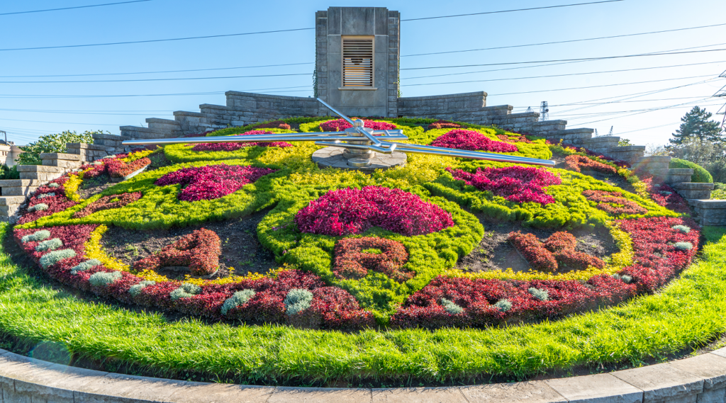 Large floral clock made of colourful flowers with a small stone tower behind