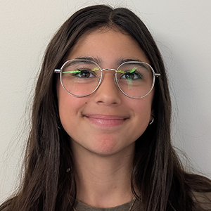 Élève aux longs cheveux foncés portant des lunettes et un chandail brun, souriant devant un fond blanc uni.