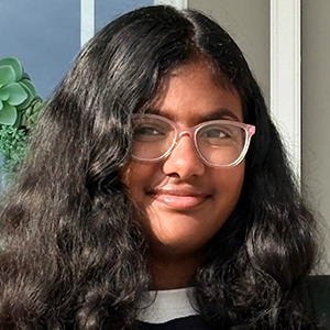 Élève aux cheveux foncés portant des lunettes, un t-shirt noir à motifs violets et blancs sur un chandail blanc à manches longues.
