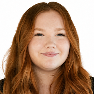 Élève aux longs cheveux roux ondulés portant un haut noir, souriant légèrement devant un fond blanc uni.